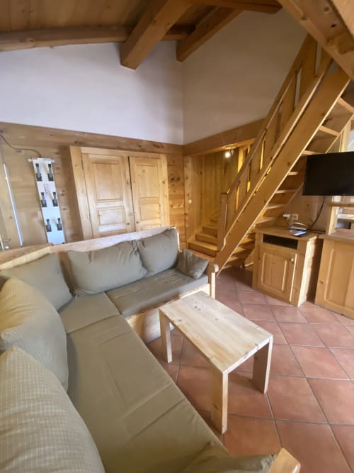 Salon cosy en bois avec canapé beige, table basse et escalier en bois à La Ferme des Georgières,