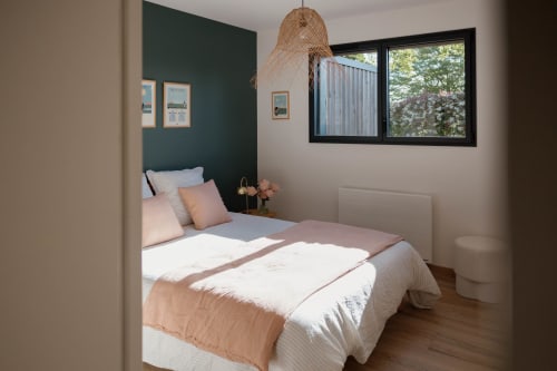 Chambre moderne du Manoir de la Nogrie avec mur accentué vert, luminaire suspendu tressé et vue sur le jardin