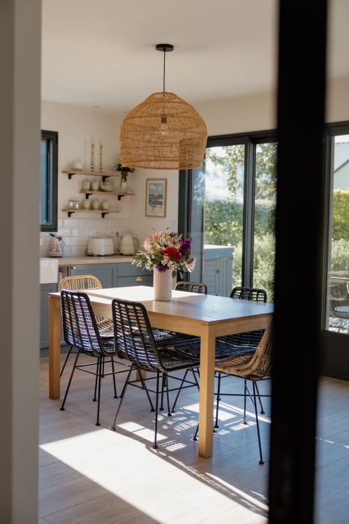 Salle à manger contemporaine du Manoir de la Nogrie avec lampe suspendue tissée, table en bois et vue sur la cuisine