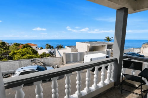 Varanda da villa Atlantic Escape com vista para o mar, corrimãos brancos, carros estacionados, edifícios brancos modernos e horizonte oceânico