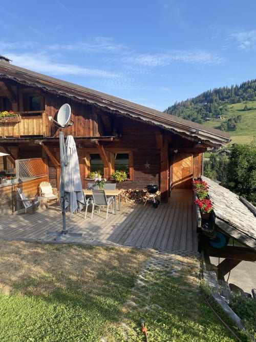 Terrasse en bois du chalet avec vue sur les montagnes, mobilier extérieur et parasol à La Ferme des Georgières