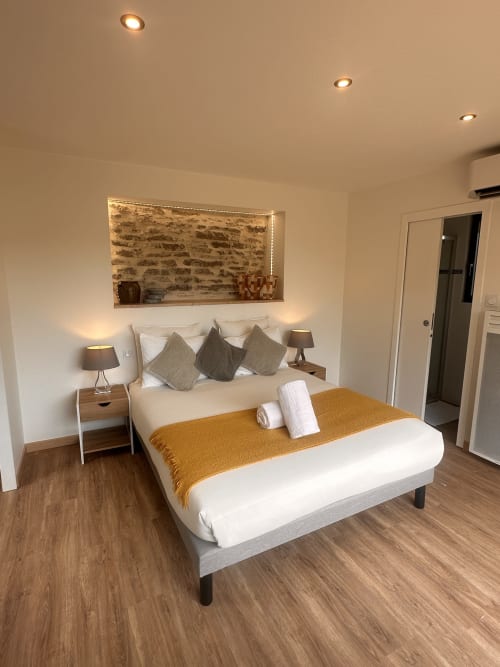 Chambre moderne au Gîte l'Harmonie du Causse avec lit queen-size, plaid ocre, tables de nuit chauffantes et alcôve en briques illuminée