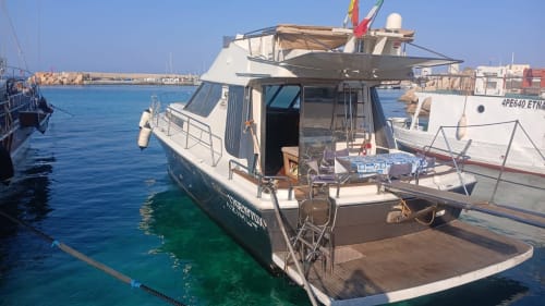 Motobarca ormeggiata nel porto di Lampedusa con acque turchesi cristalline e villaggio costiero sullo sfondo