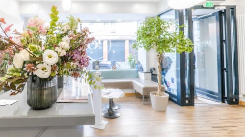 Lobby moderne de l'Hôtel d'Orléans avec composition florale fraîche, zone de détente et portes d'entrée vitrées à Orléans
