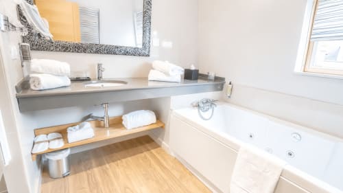 Salle de bains moderne de l'Hôtel d'Orleans avec vasque grise, serviettes blanches, étagères en bois et baignoire balnéo
