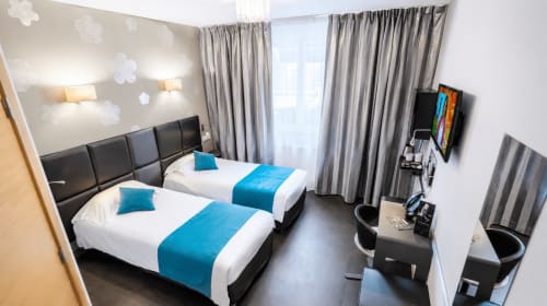 Chambre twin moderne à l'Hôtel d'Orléans avec art mural nuageux, rideaux gris, accents bleus et bureau de travail