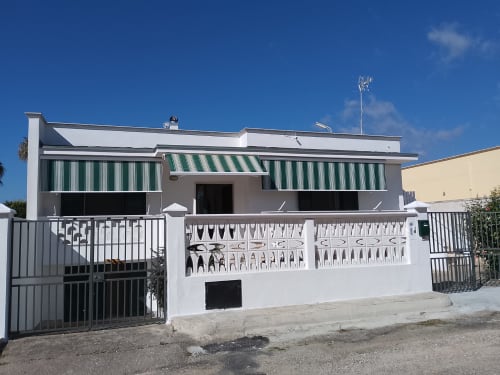 Villa Casa Alba a Torre Lapillo con facciata bianca, tende verdi a righe e ingresso con cancellata decorativa