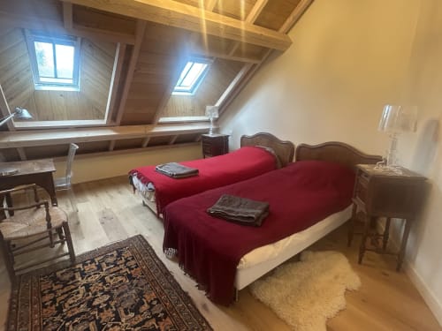 Chambre mansardée à la Cour Du Liège avec deux lits jumeaux, draps rouges, puits de lumière et poutres en bois