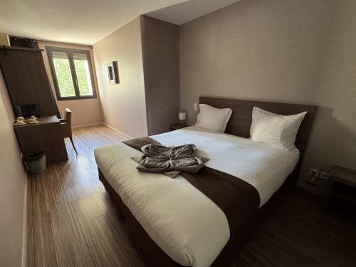 Modern double bedroom at Hôtel de la Bourse in Bagnols-sur-Cèze with white linens, dark headboard, and city view balcony