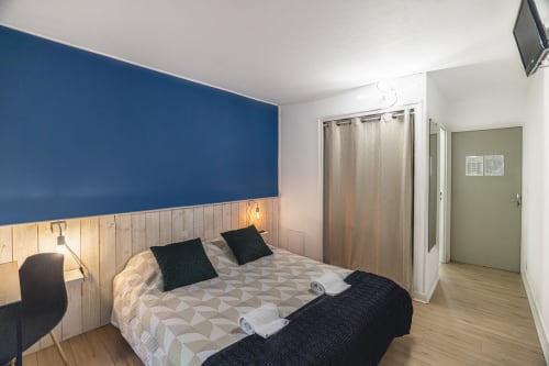Chambre double à l'Hôtel De La Bonnheure à Bracieux avec mur d'accent bleu, tête de lit en bois et vue sur le jardin
