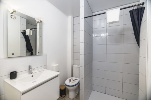 Salle de bains moderne à l'Hôtel De La Bonnheur avec lavabo blanc, douche carrelage gris et rideau noir