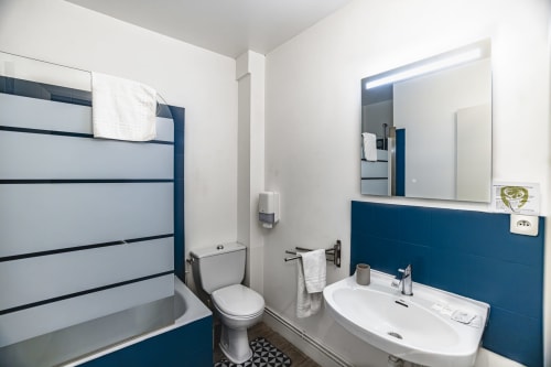 Salle de bain moderne de l'Hôtel De La Bonnheur Bracieux avec décor bleu marine et blanc, lavabo, miroir et baignoire-douche.