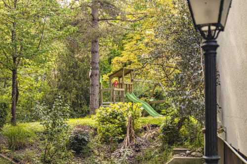 Vue luxuriante du jardin de l'appartement Hôtel De La Bonnheur avec aire de jeux et grands arbres à Bracieux