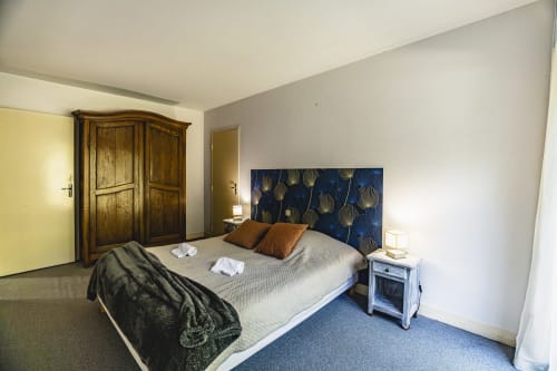 Spacieuse chambre à l'Hôtel De La Bonnheure avec tête de lit fleurie bleue, armoire en bois et vue sur le jardin