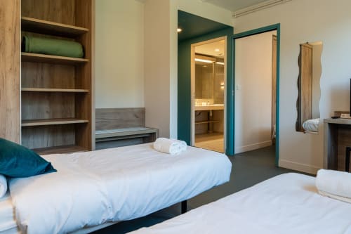 Chambre quadruple moderne à la Maison Du Haut Salat à Seix avec deux lits, salle de bains attenante, étagères en bois et accents bleu-vert