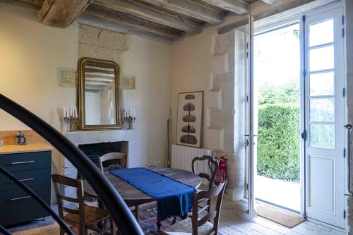Chambre du cottage Le Fruitier à la Cour Du Liège avec table bleue, cheminée, miroir et portes donnant sur le jardin