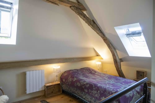 Chambre rustique aux poutres apparentes, literie violette, lucarnes et radiateur blanc du gîte Cour Du Liège.