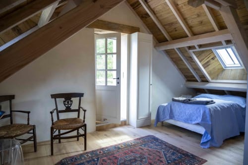 Chambre mansardée lumineuse à la Cour Du Liège avec poutres apparentes, literie bleue, chaises en bois et vue sur le jardin par les velux