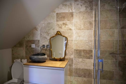 Salle de bain moderne du cottage Le Studio à Cour Du Liège avec murs en pierre, lavabo noir, miroir doré et