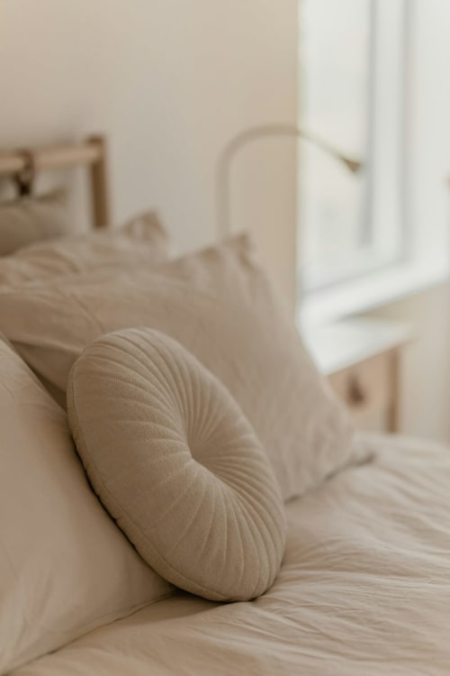 Chambre accueillante de l'hôtel L'escapade au Mans avec coussins crème et lumière naturelle