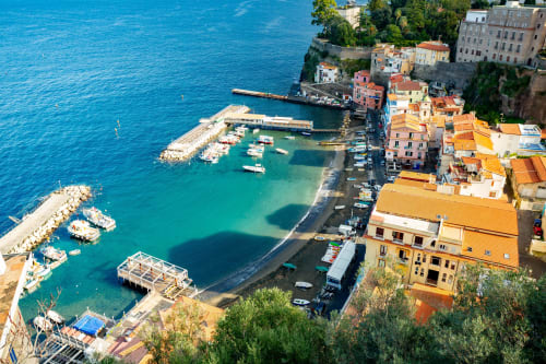 Vista aerea del B&B Anima Est in Italia con edifici colorati, mare Mediterraneo turchese e barche ormeggiate sulla costa