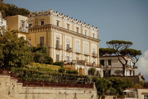 Anima Est B&B in Italia, elegante palazzo giallo con balconate ornamentali e giardini mediterranei su pendio collinare