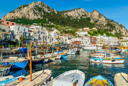 Coloratissime barche da pesca nel porto di Capri con scogliere calcaree spettacolari e edifici fronte mare, location dell'hotel Anima Est.