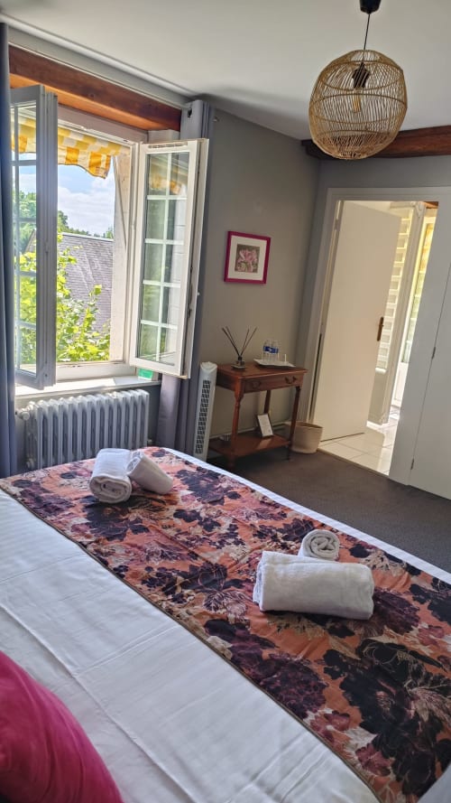 Spacious bedroom at Le Moulin de Bacchus in Chancay with rolled towels on floral runner, open window with river view, woven