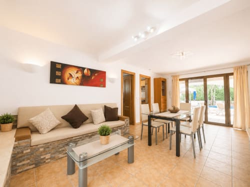 Moderna sala de estar en villa Casa Jonur, Moraira con sofá beige, comedor, baldosas de terracota y vistas al mar a través de cristaleras