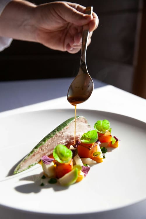 Chef versant une sauce sur un poisson dressé accompagné de légumes au restaurant L'escapade au Mans