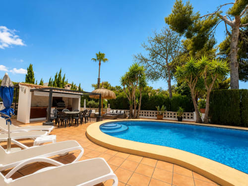 Moraira villa pool with lounge chairs, dining area, and palm trees under clear sky