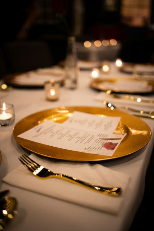 Installation élégante de salle à manger à l'hôtel L'escapade au Mans : assiette dorée, menu et table éclairée aux chandelles