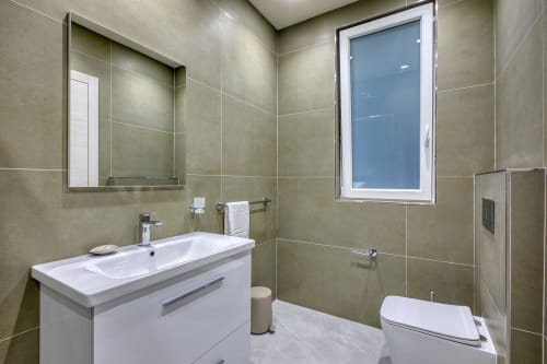 Moderno bagno a Marea Sliema con lavabo bianco, pareti piastrellate, specchio, WC e finestra affacciata sulla corte a Sliema