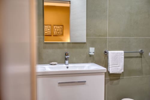 Moderno bagno con lavabo bianco, piastrelle verdi, specchio illuminato e porta asciugamani all'hotel Marea Sliema, Sliema