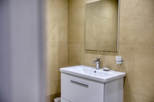 Bagno moderno nella Marea Sliema Seaview Room con vanità bianca, pareti piastrellate beige e specchio a Sliema, Malta
