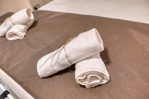 Asciugamani bianchi arrotolati legati con spago su un letto beige all'hotel Marea Sliema a Malta