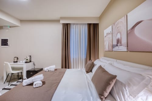 Camera moderna a Marea Sliema con letto queen size, macchina da caffè, scrivania e finestra con tende marroni che affacciano sulla corte