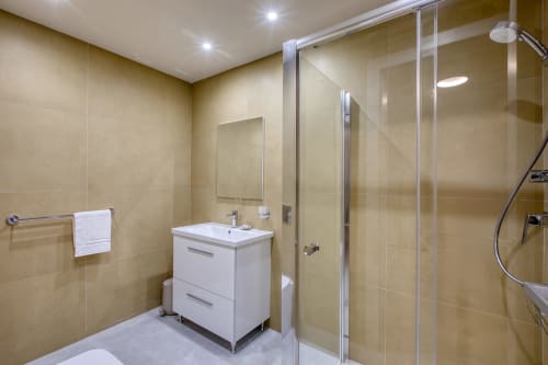 Bagno moderno a Marea Sliema con vanity bianco, doccia in vetro e pareti rivestite di piastrelle beige