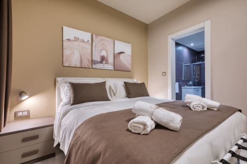 Camera da letto elegante a Marea Sliema con letto king size, accenti marrone, bagno ensuite moderno e opere d'arte con vista città