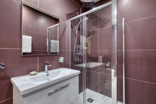 Bagno moderno dell'hotel Marea Sliema con piastrelle bordeaux, lavabo bianco, box doccia in vetro e specchio con portasciugamani