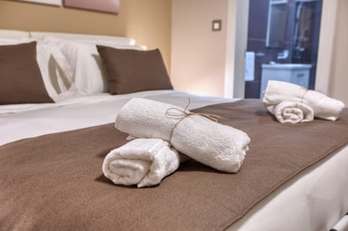 Asciugamani bianchi arrotolati legati con spago su biancheria marrone nella Room Breeze 4 dell'hotel Marea Sliema a Sliema.