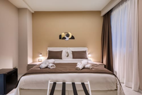 Camera elegante a Marea Sliema con parete in beige, biancheria bianca, cuscini marroni e opere d'arte moderna