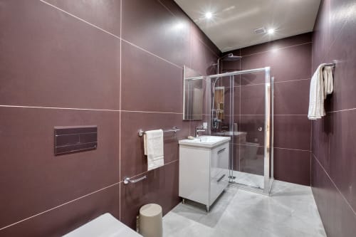 Bagno moderno a Marea Sliema con pareti in piastrelle bordeaux, vanità bianca, box doccia in vetro e scaldasalviette