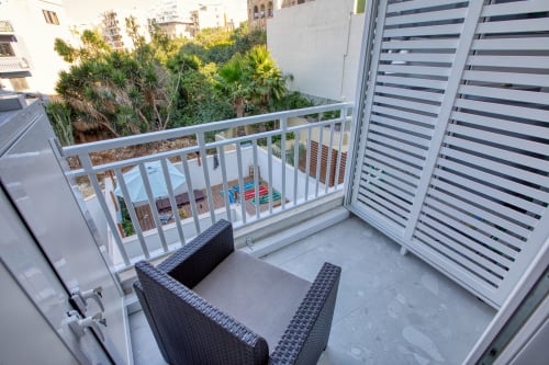 Balcone dell'appartamento Marea a Sliema con ringhiere bianche, lettini, schermo privacy a righe e vista su palme