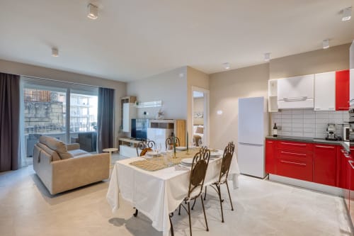 Moderno appartamento open-plan a Marea Sliema con cucina rossa, tavolo da pranzo, divano beige e balcone con vista mare a Sliema.