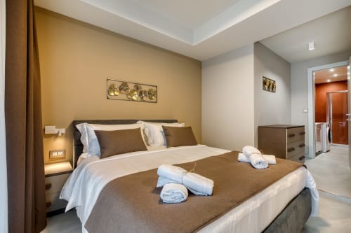 Camera moderna a Marea Sliema con parete accento dorato, letto king, asciugamani arrotolati e bagno en-suite con vista mare