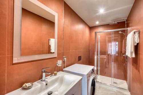Bagno moderno a Marea Sliema con piastrelle in terracotta, lavabo bianco, box doccia in vetro e lavatrice.