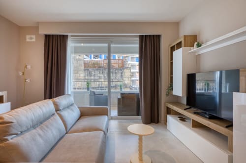 Elegante appartamento con vista mare a Marea Sliema: divano beige, TV a schermo piatto, scaffalature in legno e balcone affacciato su Sliema