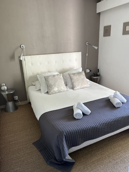 Modern hotel bedroom with white tufted headboard, dark quilted bedcover, rolled towels, and neutral décor at Hôtel