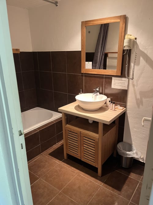 Modern bathroom with dark tile, wooden vanity with white basin, mirror, bathtub at Hôtel l'Orangeraie Lavandou